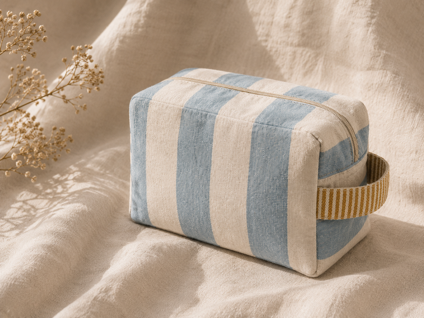 neceser mediterráneo de rayas azules y beige sobre lino arrugado iluminado por el sol